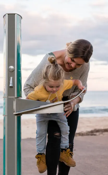 A woman with her daughter using Aquafil Drinking Water Stations installed near beach shore