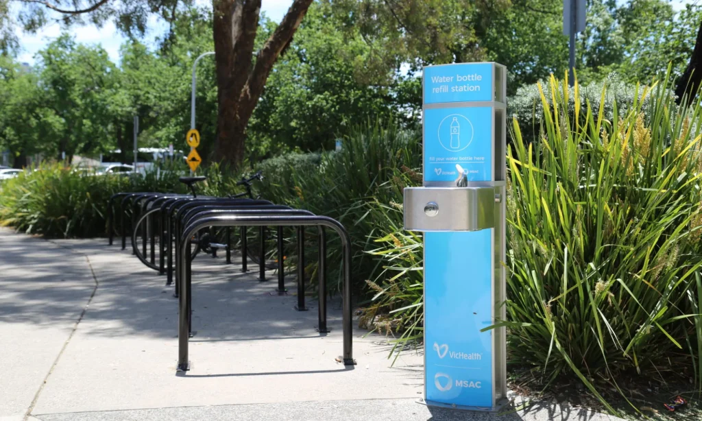 Drinking fountain and water bottle refill station with blue artwork and a set of bike racks installed at Melbourne Sports and Aquatic Centre