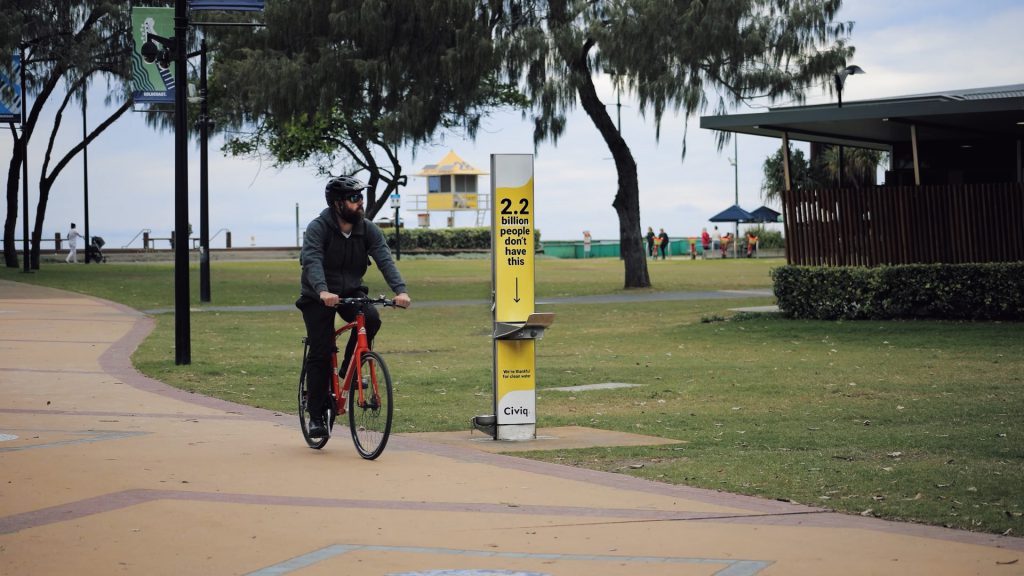 A man riding his bicycle beside of a drinking water station installed in a public park
