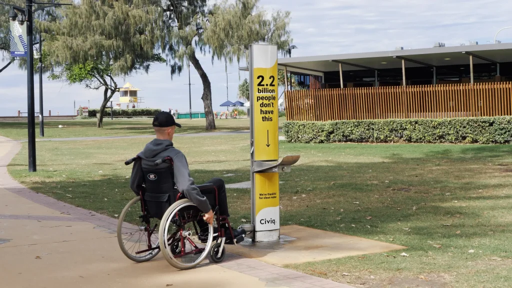 A man in a wheelchair accessing a drinking water station installed in a public park