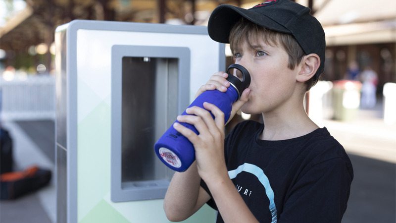 a child drinking on his water bottle with the Aquafil Portable Bottle Refilling Station in the background