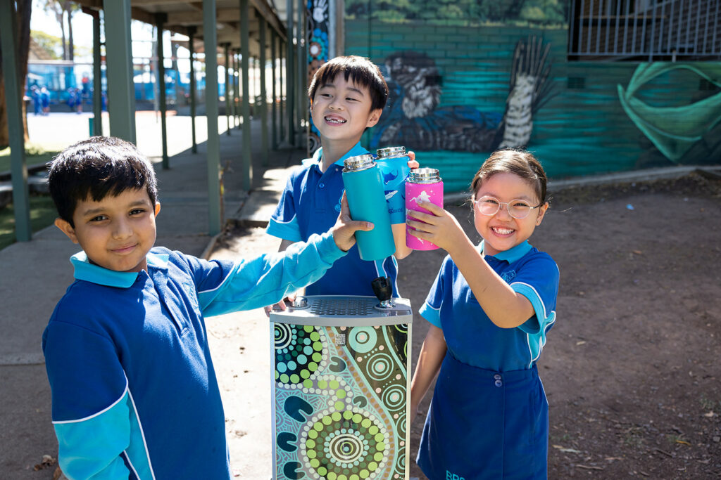 School children with smiles on their faces as they stay hydrated at the newly installed school bubbler, adorned with an updated artwork template that encourages a healthy and sustainable lifestyle.