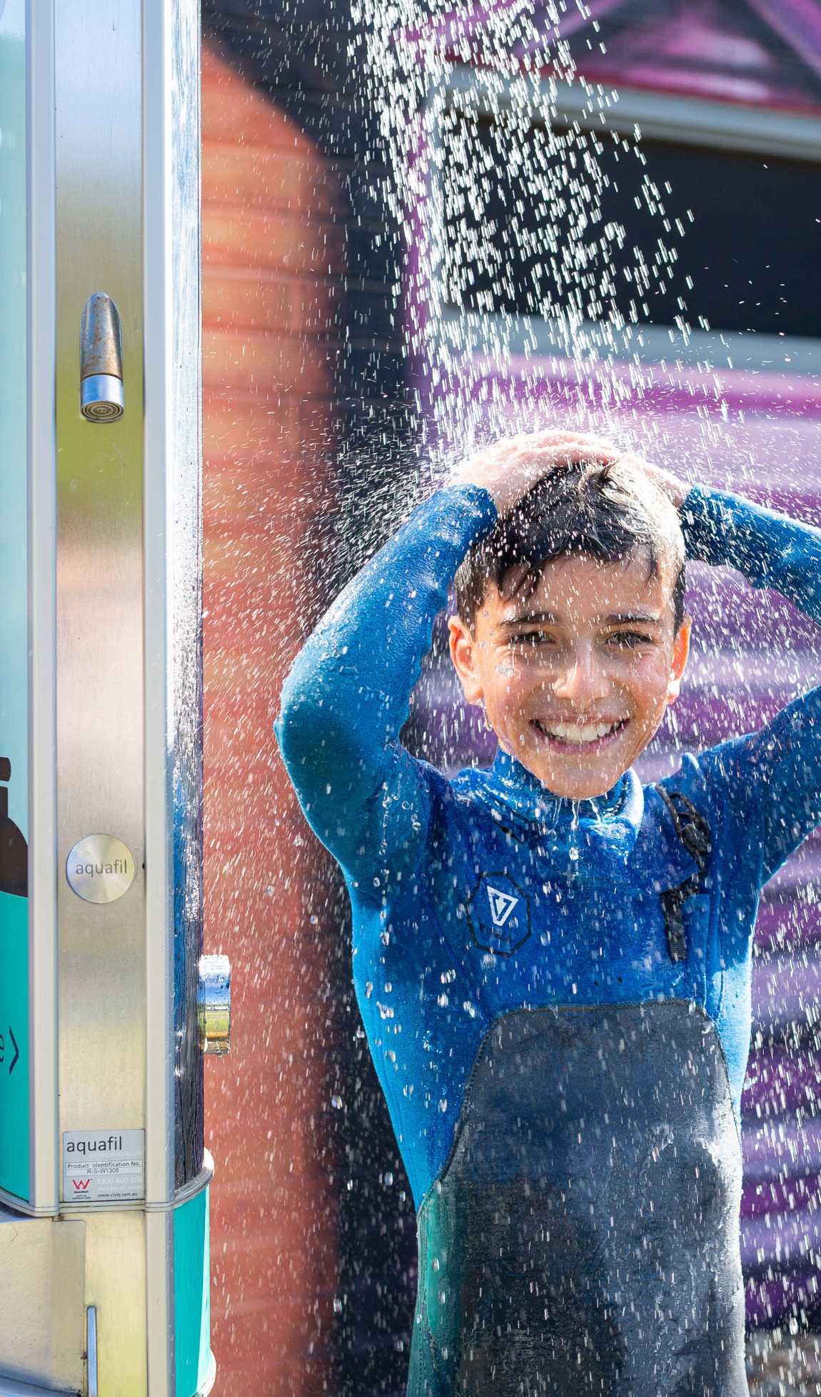 A guest savoring the refreshing convenience of the Civiq Aquafil Outdoor Shower at Culburra Beach Holiday Haven, which includes a drinking fountain and bottle refilling station, providing a handy way for beachgoers to cleanse and stay refreshed.
