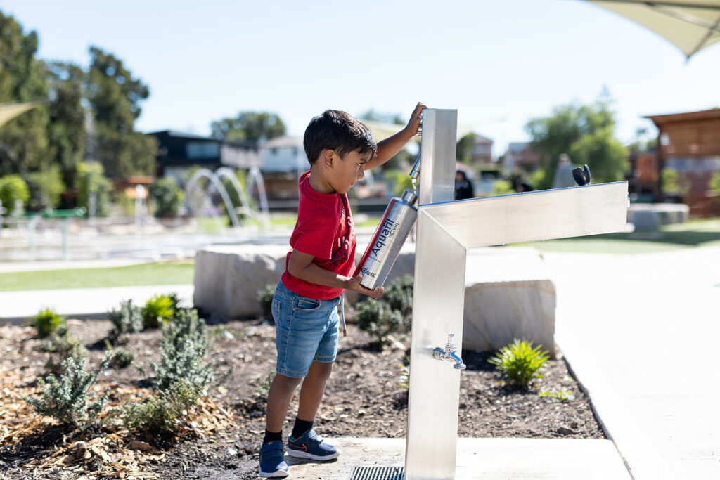 A boy refilling his water bottle at an Aquafil Bold, a stainless steel drinking fountain and water bottle refill station installed at a community park.