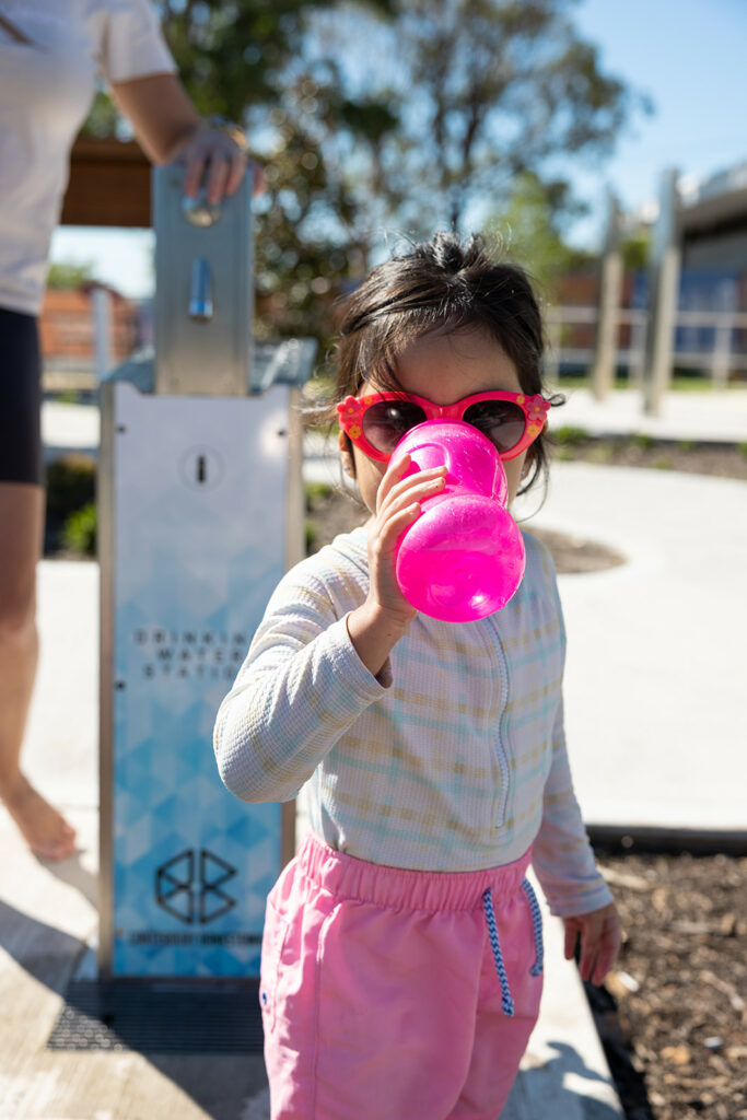 A child drinking from her water bottle with Aquafil Bold Drinking Fountain on the background