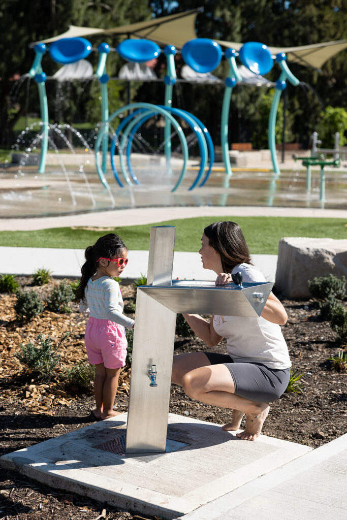 A mother and her child utilising Aquafil Bold drinking fountain and water bottle refilling station installed at The Greenacre Splash Park 