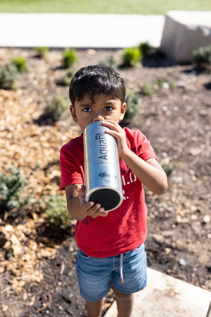 A young boy takes a refreshing sip from his trusty water bottle with Aquafil logo, quenching his thirst on a sunny day.