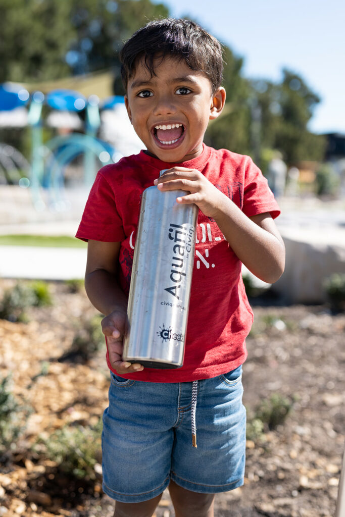 A happy child proudly holds a water bottle featuring an Aquafil logo, ready to stay hydrated and enjoy their day!