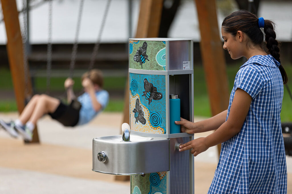 A student replenishes her water bottle at an Aquafil Pulse Drinking Fountain and Water Bottle Refilling Station, featuring captivating new Aboriginal Artwork. Combining functionality with cultural expression in one refreshing moment.
